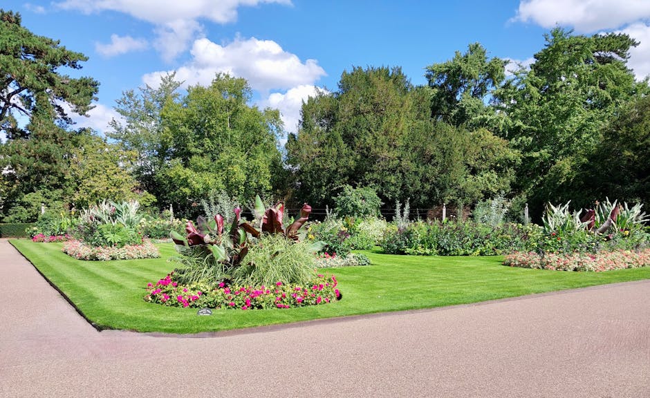 A well-maintained garden with a freshly mowed lawn featuring evenly spaced light and dark green stripes, bordered by a tall, neatly trimmed hedge on the left. Along the hedge, there are four large, we